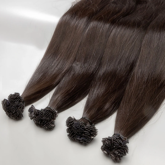 A set of brown K-tip hair extensions displayed on a surface, with each extension featuring a floral-like knot at the end.
