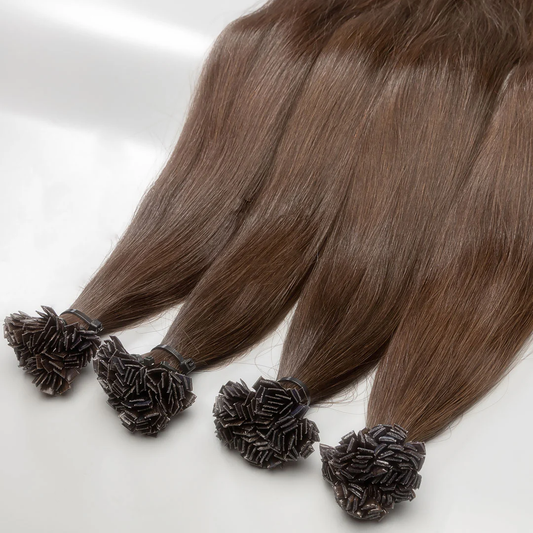 A section of light brown, curly hair extensions with a keratin bond, displayed on a white surface.