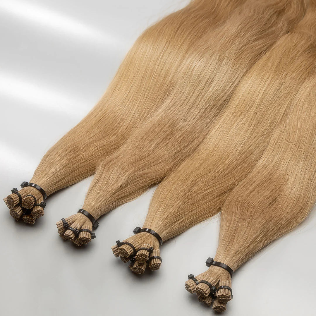 A photo of I-tip hair extensions with a dark blonde color, displayed in a way that shows the tips and the length of the strands.