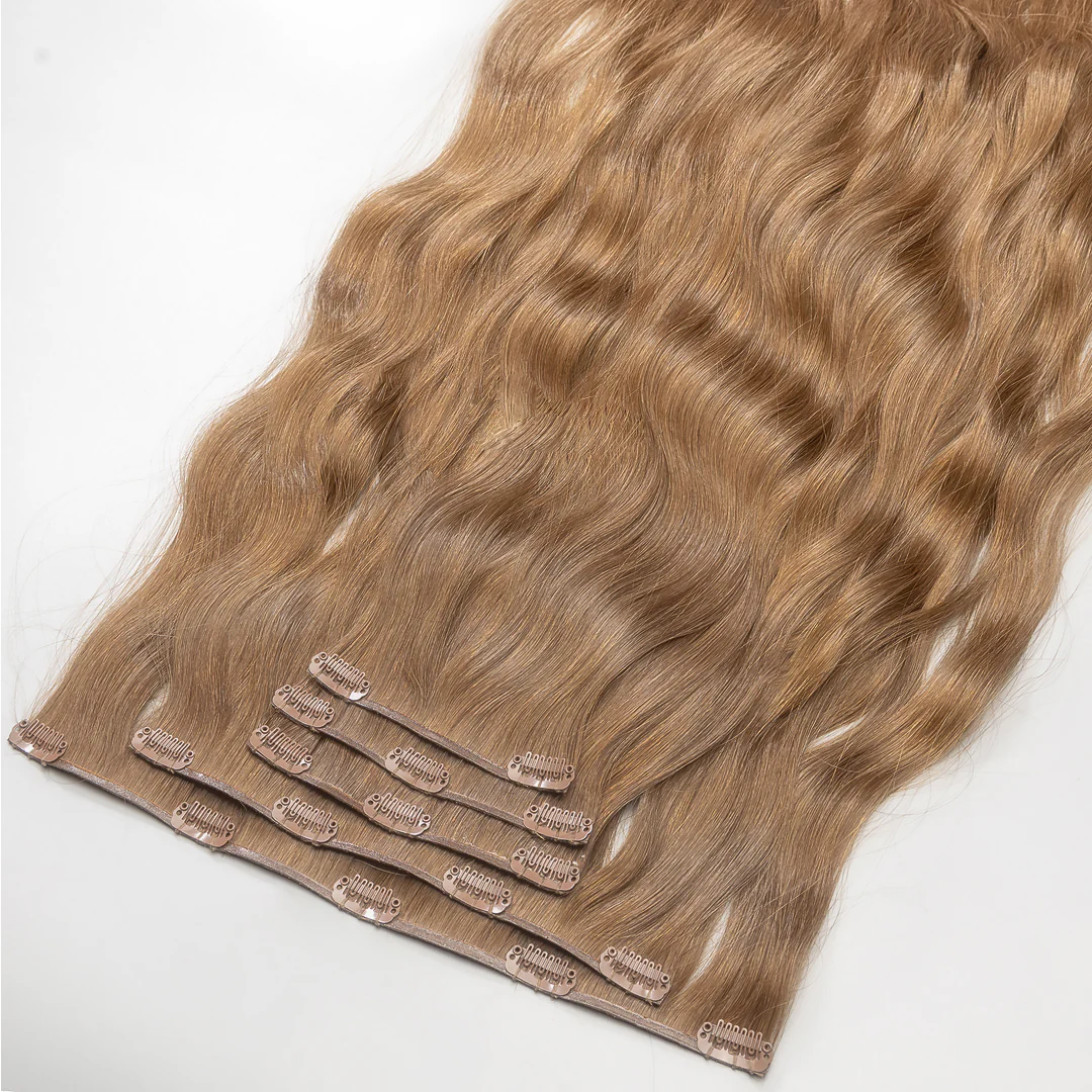 A section of clip-in hair extensions with a golden dark blonde color, attached to small metal clips.