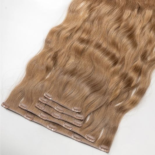 A section of clip-in hair extensions with a golden dark blonde color, attached to small metal clips.