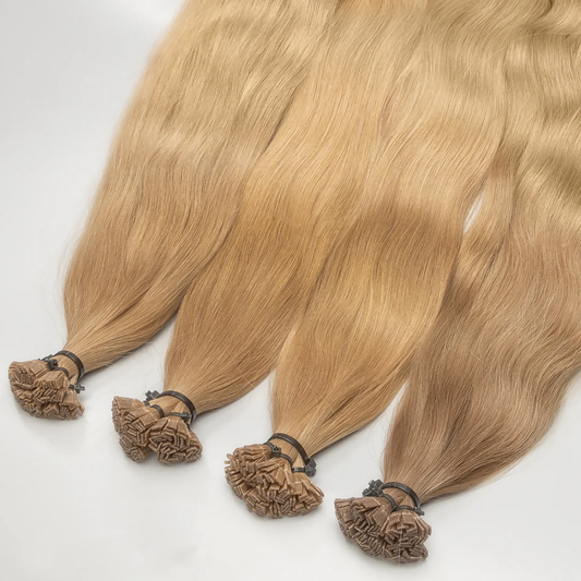A set of golden blonde K-tip hair extensions with keratin bonds, displayed on a white surface.