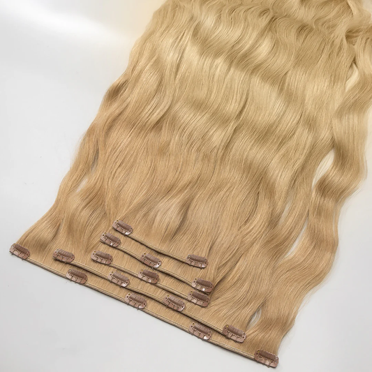 A section of clip-in, golden blonde hair extensions with visible clips and weaves.