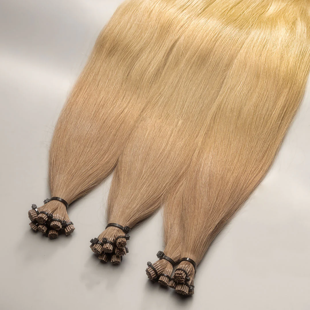 A pair of golden blonde hair extensions with I-tip caps, displayed on a light surface.