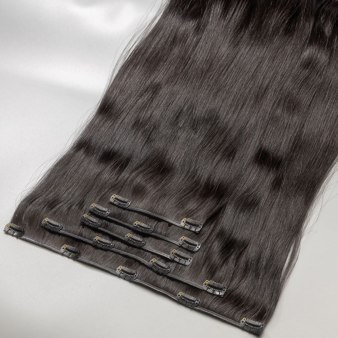A section of darkest brown clip-in hair extensions attached to small metal clips, laid out on a light surface.