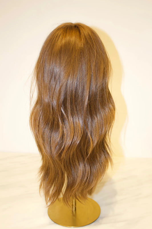A light brown wig on a mannequin head, displaying natural-looking hair texture and a pre-plucked hairline with baby hairs.