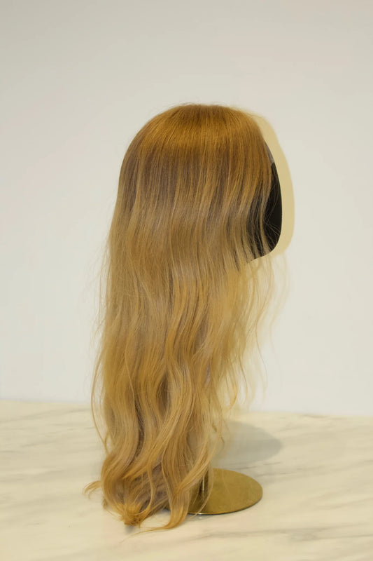 A wig with a golden blonde color, displayed on a mannequin head, with the mannequin's head not shown.